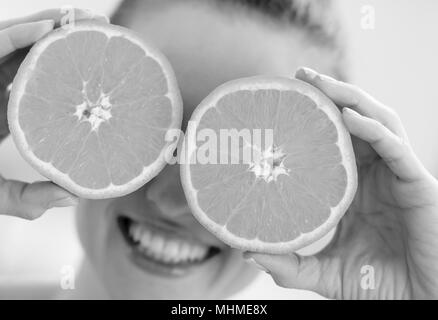 Happy young woman holding deux tranches d'orange en face des yeux Banque D'Images