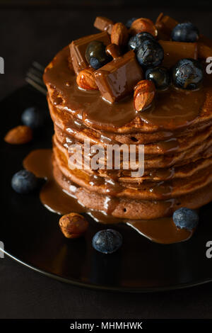 Pile de crêpes au chocolat avec du glaçage, de bleuets, d'amandes, de noisettes et de chocolat. Focus sélectif. Banque D'Images