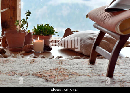 Salle de pause avec chaise, plantes et bougie devant des fenêtres triples vitrage dans un chalet de montagne Banque D'Images