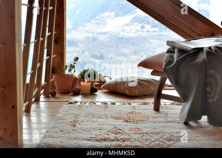 Salle de pause avec chaise, plantes et bougie devant des fenêtres triples vitrage dans un chalet de montagne Banque D'Images