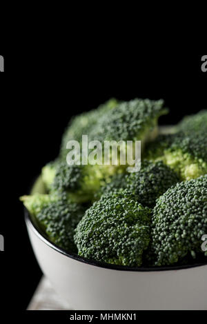 Libre de quelques tiges de brocoli dans un bol en céramique blanc, sur une table en bois rustique, d'un fond noir Banque D'Images
