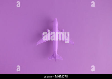Mise à plat de l'avion jouet miniature sur fond violet voyage minime et les concepts créatifs. Banque D'Images