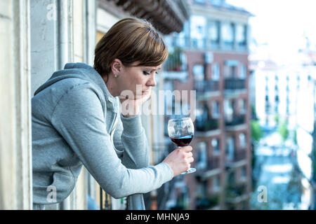 Belle red haired woman souffrant de dépression tenant un verre de vin sur un balcon à la maison. Staring out sentiment de tristesse, de douleur et de chagrin. Banque D'Images