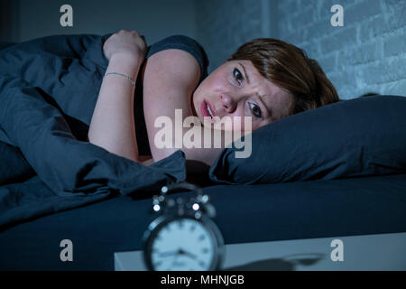 Les jeunes aux cheveux rouge attrayante caucasian woman au lit tard dans la nuit à essayer de dormir souffrant d'insomnie, cauchemars ou troubles du sommeil. Banque D'Images