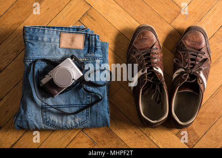 Une paire de jeans bleu frettées, chaussures brunes, et un mensonge par caméra sur le sol. Banque D'Images