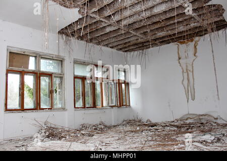 Chambre à l'immeuble abandonné avec des fenêtres cassées, détruit les planches pleine de décombres, les murs avec l'humidité des patchs et isolation du plafond suspendu Banque D'Images