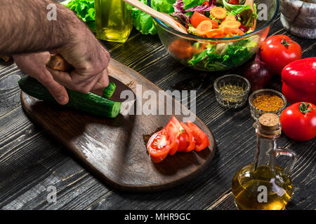 L'homme est de couper le concombre dans la cuisine dans sa maison pour préparer le dîner manger avec une salade. Banque D'Images