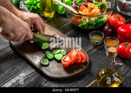 L'homme est de couper le concombre dans la cuisine dans sa maison pour préparer le dîner manger avec une salade. Banque D'Images