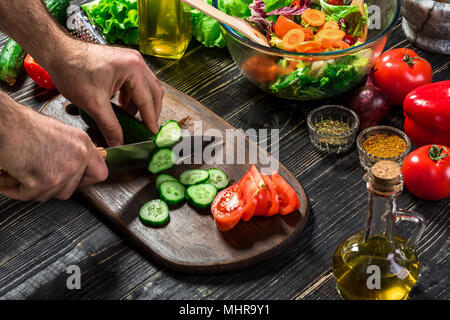 L'homme est de couper le concombre dans la cuisine dans sa maison pour préparer le dîner manger avec une salade. Banque D'Images