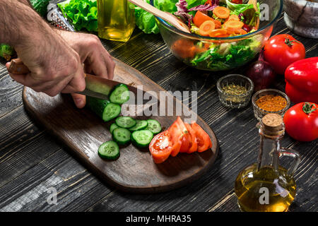 L'homme est de couper le concombre dans la cuisine dans sa maison pour préparer le dîner manger avec une salade. Banque D'Images