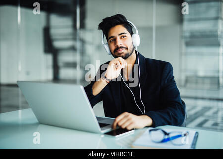 Jeune homme d'affaires travaillant avec un ordinateur portable et casque au bureau, symbolisant le support client Banque D'Images