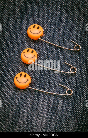 Les broches métalliques de sécurité en plastique fixée en matière de jeans. Emoticon sourire orange de la goupille de sécurité. Mignon et drôle des émoticônes colorées. Banque D'Images