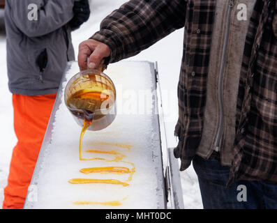 Un homme liquide chaud couler le sirop d'érable sur la glace, où il se refroidit pour former de la tire Banque D'Images