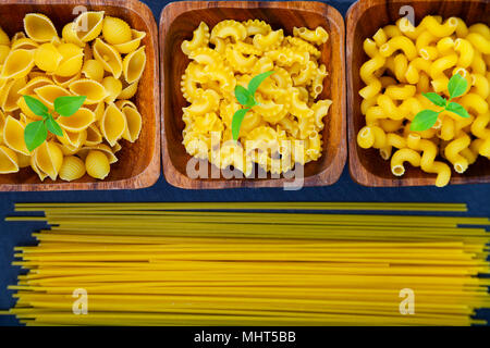 Divers les pâtes dans des bols en bois sombre sur un fond de bois. Pâtes crues et basilic close-up. Banque D'Images