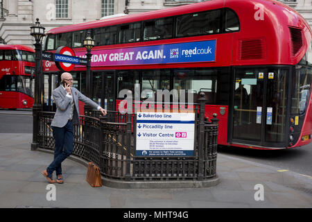 Un jeune homme bien habillé sur son téléphone tout en se penchant sur les garde-corps à une entrée de la station de métro Piccadilly Circus le 1er mai, à Londres, en Angleterre. Banque D'Images