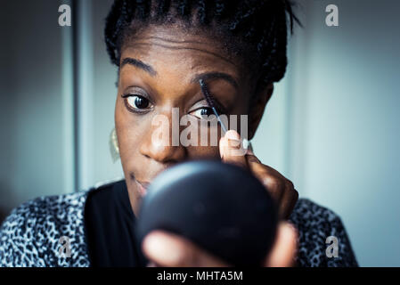 Femme noire de la préparation pour une nuit, appliquant le maquillage dans un miroir à main Banque D'Images