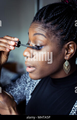 Femme noire de la préparation pour une nuit, appliquant le maquillage dans un miroir à main Banque D'Images