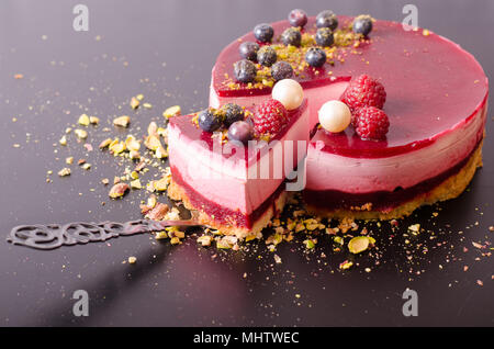 Morceau de gâteau framboise délicieux avec des fraises, framboises, bleuets, raisins secs et pistaches sur pelle, fond noir. Espace libre pour votre texte. Banque D'Images