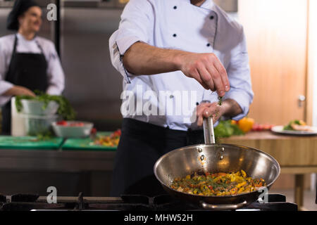 Young male chef mettre les épices sur les légumes dans le wok à cuisine commerciale Banque D'Images