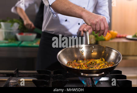 Young male chef mettre les épices sur les légumes dans le wok à cuisine commerciale Banque D'Images