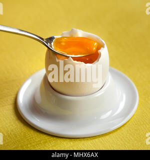 Oeufs à la coque dans un coquetier en porcelaine avec une cuillère à café sur fond jaune. Banque D'Images