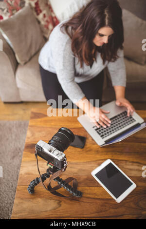 Vlogger femelle sitting on sofa while using laptop Banque D'Images