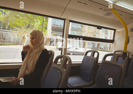 Hijab femme parlant sur tablette numérique tout en voyageant en bus Banque D'Images