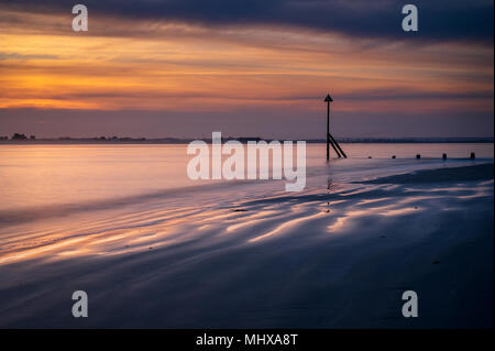 Belle soirée de printemps à West Wittering avec la marée marée ciel nuageux au coucher du soleil chaud de l'eau lisse avec quelques ondulations et ridée de sable Banque D'Images