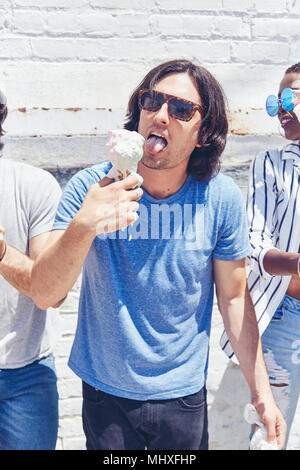 Jeune homme léchant melting ice cream cone, cropped Banque D'Images