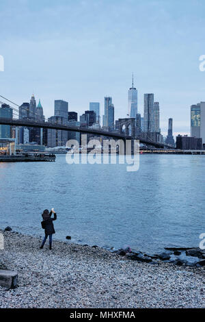 Woman photographing Pont de Brooklyn et Manhattan Skyline à partir de la berge, New York, USA Banque D'Images