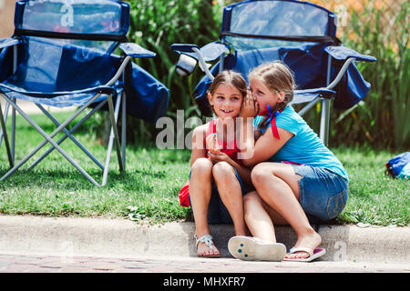 Deux jeunes filles girl sitting on curb, chuchotant à l'oreille d'amis Banque D'Images