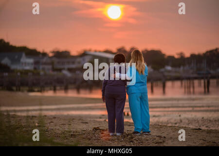 Femme et les personnes chargées d'apprécier le coucher du soleil en soirée par la mer Banque D'Images