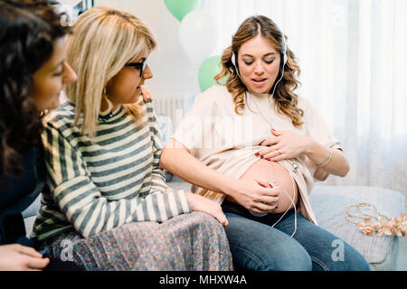 Femme enceinte et amis le canapé à l'aide d'écoute prénatale Banque D'Images