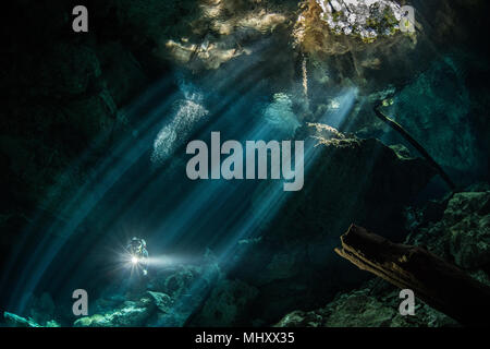 Plongeur mâle plongée dans une rivière souterraine (cenote) avec les rayons du soleil et les formations rocheuses, Tulum, Quintana Roo, Mexique Banque D'Images