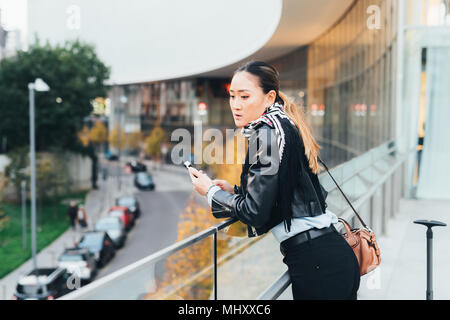 Femme, à l'extérieur, appuyé sur des balustrades, holding smartphone Banque D'Images
