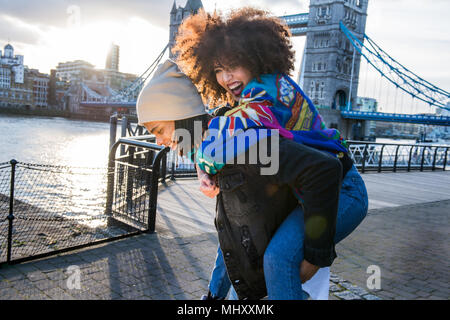 Donner aux jeunes les jeunes woman piggyback en plein air, le Tower Bridge en arrière-plan, London, England, UK Banque D'Images