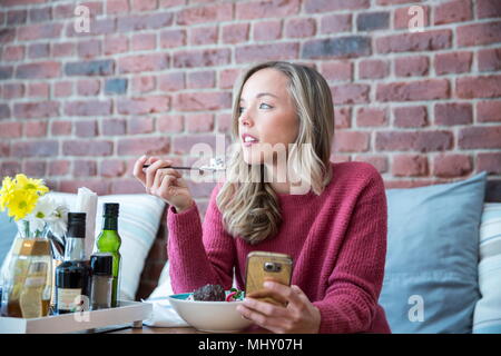 Woman sitting in cafe, manger bol de muesli, holding smartphone Banque D'Images