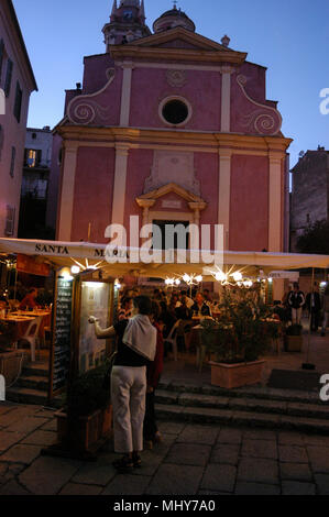 Les touristes de la lecture d'un menu de restaurant à l'un des nombreux restaurants en face de l'église Sainte-Marie-Majeure ou l'Église Sainte-Marie de Calvi en place du Dr Banque D'Images