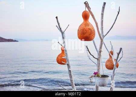 La main de décoration de citrouille d'eau (gourde calebasse) lampes suspendu à un arbre blanc en face d'une mer calme au lever du soleil d'arrière-plan Banque D'Images