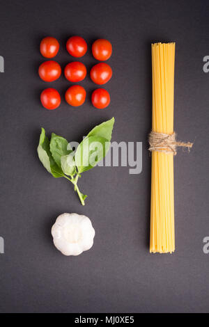 Recette culinaire concept. Spaghettis attachés avec une corde avec des tomates cerises, de l'ail et basilic sur fond noir. Mise à plat Banque D'Images