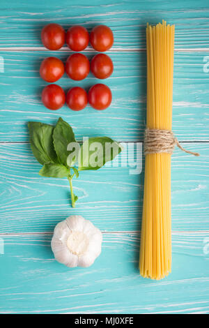 Mise à plat de spaghetti ingrédients : pâtes, l'ail, basilic et tomates fraîches sur fond de bois bleu Banque D'Images