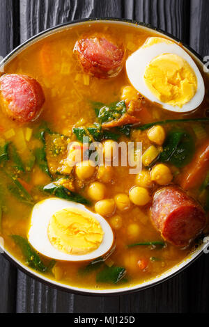 Soupe épicée aux épinards, pois chiches, chorizo saucisses, œufs durs close-up dans un bol sur la table. Haut Vertical Vue de dessus Banque D'Images
