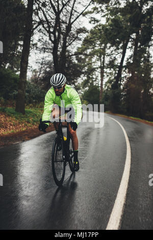 Cycliste homme équitation vélo sur route de campagne un jour de pluie. Monter sportsman dans gaine verte à vélo sur route vide à travers la forêt. Banque D'Images