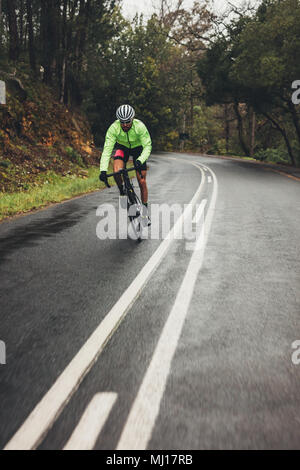 Bicycle rider riding bike sur la route d'asphalte humide en campagne. Vélo homme extérieur sur vide longue route à travers la forêt. Banque D'Images