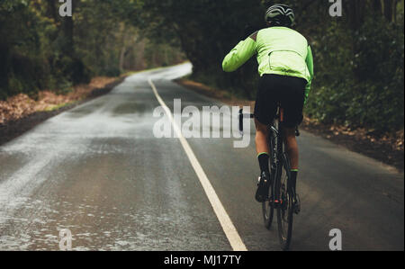 Vue arrière du vélo de l'athlète masculin on country road sur jour de pluie. Cycliste professionnel de faire du vélo sur l'autoroute à travers la forêt vide. Banque D'Images