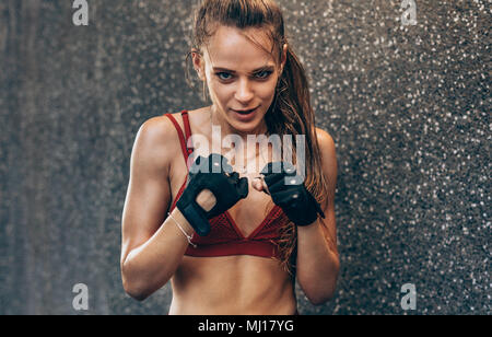 Femme portant des gants prêt à combattre. Boxer femme exerçant à l'extérieur contre le mur gris. Banque D'Images