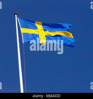 Drapeau suédois dans l'ensoleillée vent frais sur un mât contre un ciel bleu clair. Banque D'Images