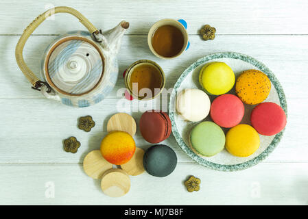 Macarons français colorés mixtes sur la plaque et table en bois avec une théière. Banque D'Images