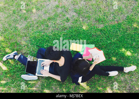 De jeunes étudiants de l'emplacement sur l'herbe verte et de la lecture en vue d'en haut. Concept de l'éducation. Banque D'Images