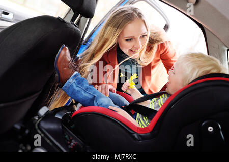 Maman met l'enfant dans le siège de la voiture et de fixer les ceintures de sécurité. Banque D'Images